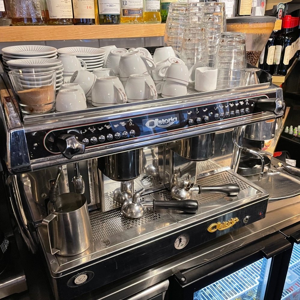 A barista checking information for troubleshooting an Astoria Gloria espresso machine in a cafe.